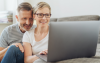 Mann und Frau sitzen mit Laptop auf Sofa.